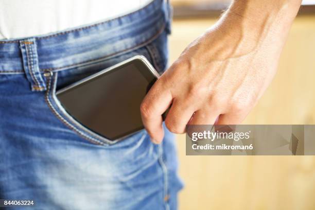 man putting mobile phone into back pocket blue jeans - jeans pocket stock-fotos und bilder