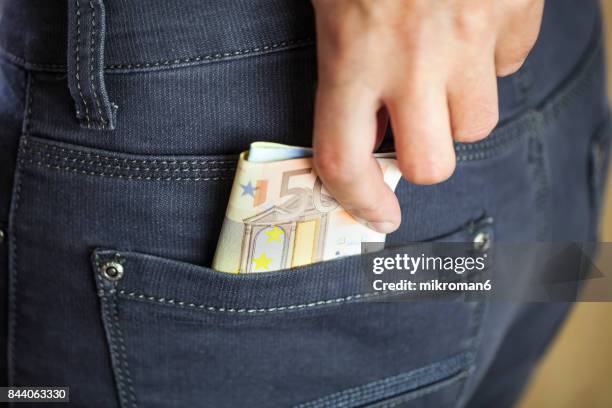 man putting a wad of cash into the pocket of his jeans - fajo de billetes de euro fotografías e imágenes de stock