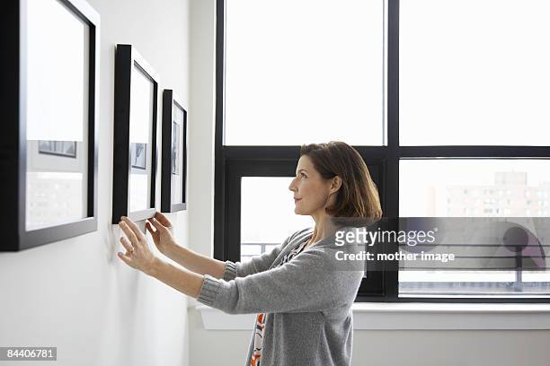 woman adjusting picture frame at home - perfezione foto e immagini stock