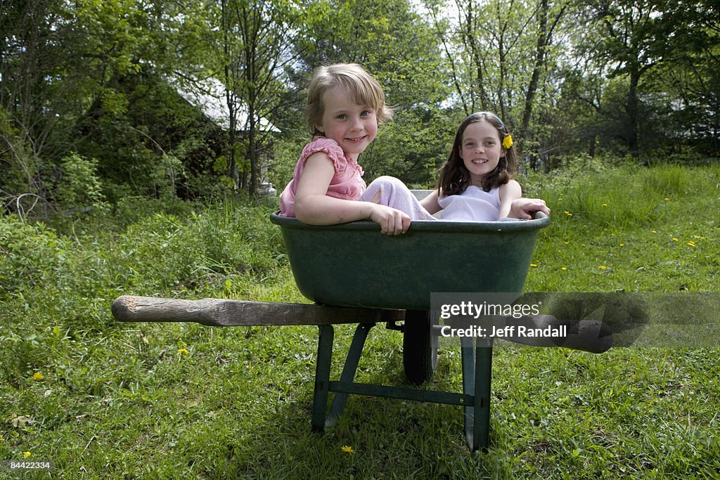 Sisters playing in wheelbarrow in back yard