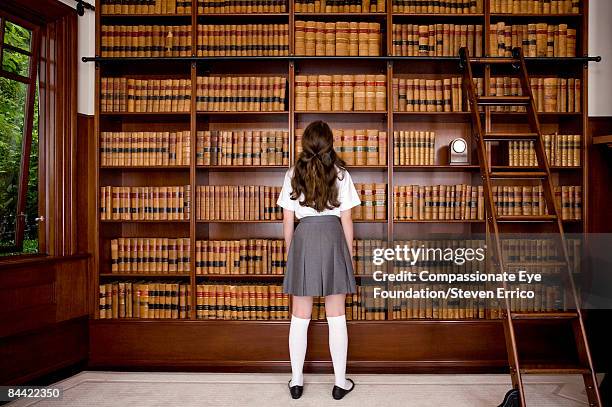 girl standing in front of bookshelves in library - school uniform stock pictures, royalty-free photos & images