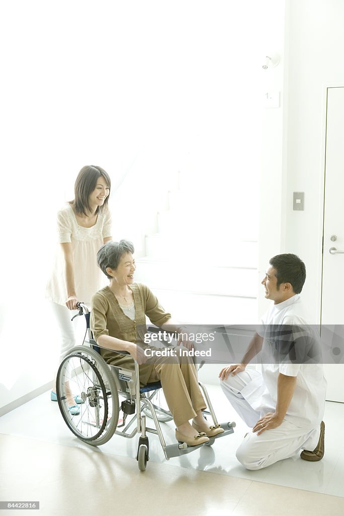 Male nurse kneeling to senior woman in wheel chair