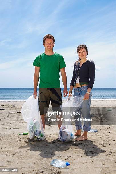 young couple collecting garbage on beach - helena price stockfoto's en -beelden