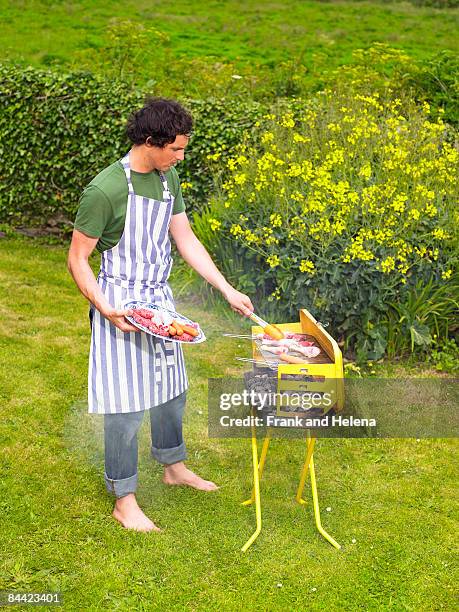 young man placing meat on barbecue - barefoot men stock-fotos und bilder