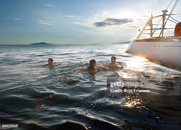 three people swimming next to sailboat - rijkdom boot stockfoto's en -beelden