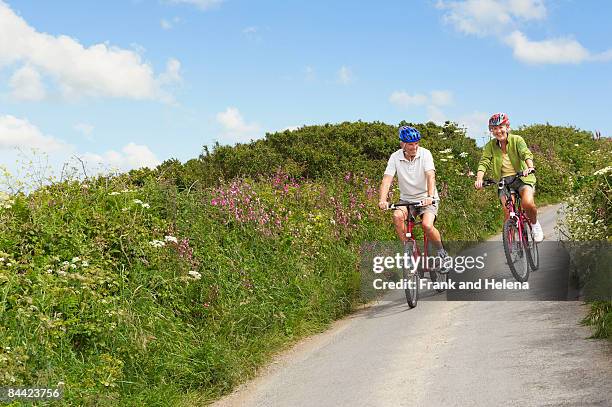 senior couple cycling down country lane - bicycle lane stock-fotos und bilder