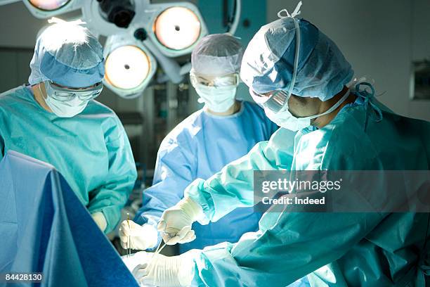 surgeons operating using surgical equipment - operating gown stock pictures, royalty-free photos & images