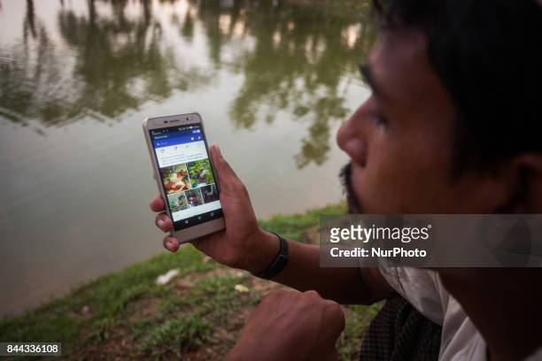 Rohingya ethnic minority man looking facebook at his cell phone at a temporary makeshift camp after crossing over from Myanmar into the Bangladesh...