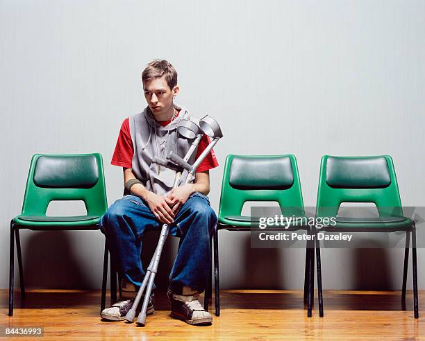 young man with crutches sitting on hospital chairs - accident hospital stockfoto's en -beelden