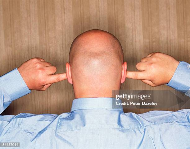 shaven headed man with fingers in ears - hand to ear photos et images de collection