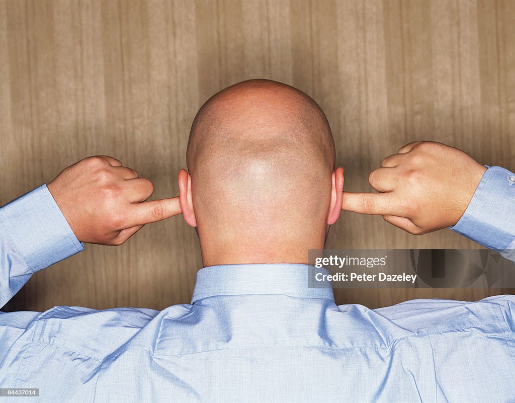 Shaven headed man with fingers in ears