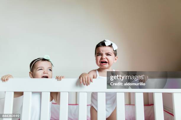 cute girl twins crying in their baby bed - crying sibling stock pictures, royalty-free photos & images