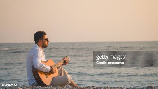 handsome man playing classic guitar sitting on the beach in vacations - acoustic music stock pictures, royalty-free photos & images