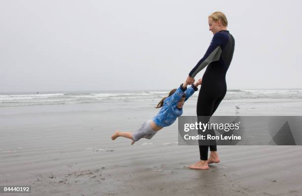 mother swinging daughter on misty beach - neoprenanzug stock-fotos und bilder