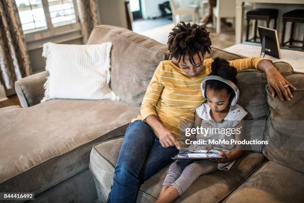 mother and daughter on couch using tablet - arts and culture imagens e fotografias de stock