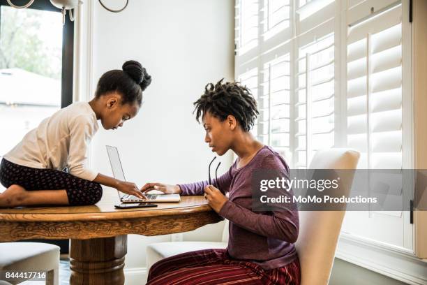 mother working on laptop, daughter on table - mãe dona de casa imagens e fotografias de stock