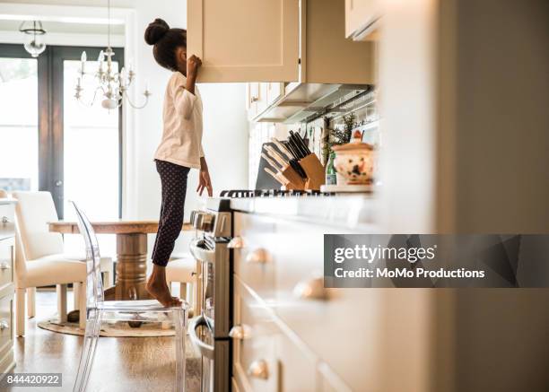 girl standing on tippy toes looking in cupboard - standing on chair stockfoto's en -beelden