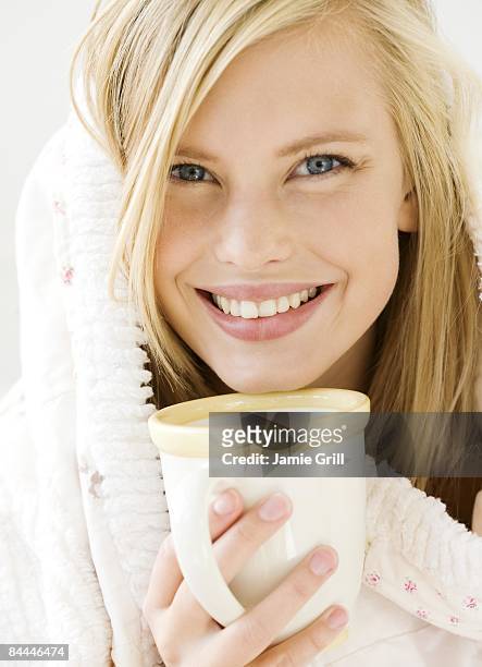 young woman wrapped in blanket with warm drink - hot blonde woman stock-fotos und bilder
