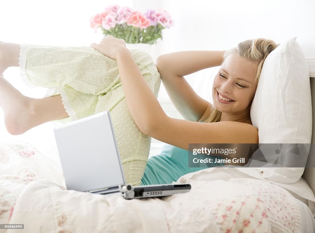 Young Woman laughing next to laptop in bed