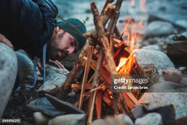 young man burning the campfire. mountainous landscape - fogueira de acampamento imagens e fotografias de stock