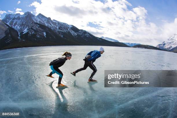 un hombre lleva a una mujer en una velocidad de invierno patinaje sobre aventura en el lago minnewanka en parque nacional banff, alberta, canadá. - skate canada fotografías e imágenes de stock