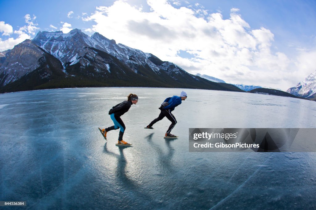 A man leads a woman on a winter speed skating adventure on Lake Minnewanka in Banff National Park, Alberta, Canada.
