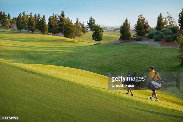 father and son carrying golf club bags - father son golf stock pictures, royalty-free photos & images