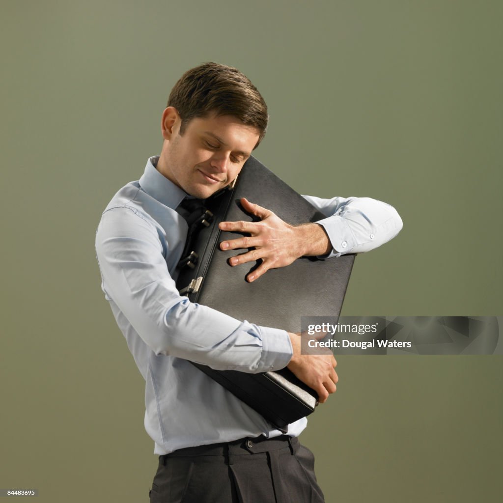 Young business man hugging briefcase.