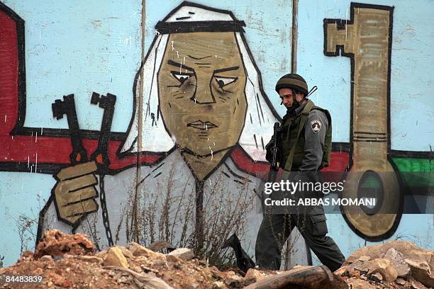 An Israeli soldier walks past the controversial separation barrier bearing a mural of an elderly Palestinian refugee holding the keys to his home,...