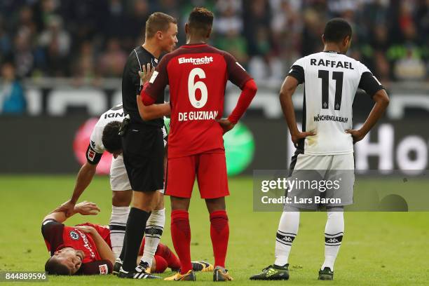 Ante Rebic of Frankfurt lies injured on the pitch while Lars Stindl of Moenchengladbach check on him, Jonathan de Guzman of Frankfurt talks to...