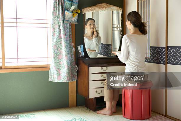 mature woman applying makeup, looking at mirror - vanity table stock pictures, royalty-free photos & images