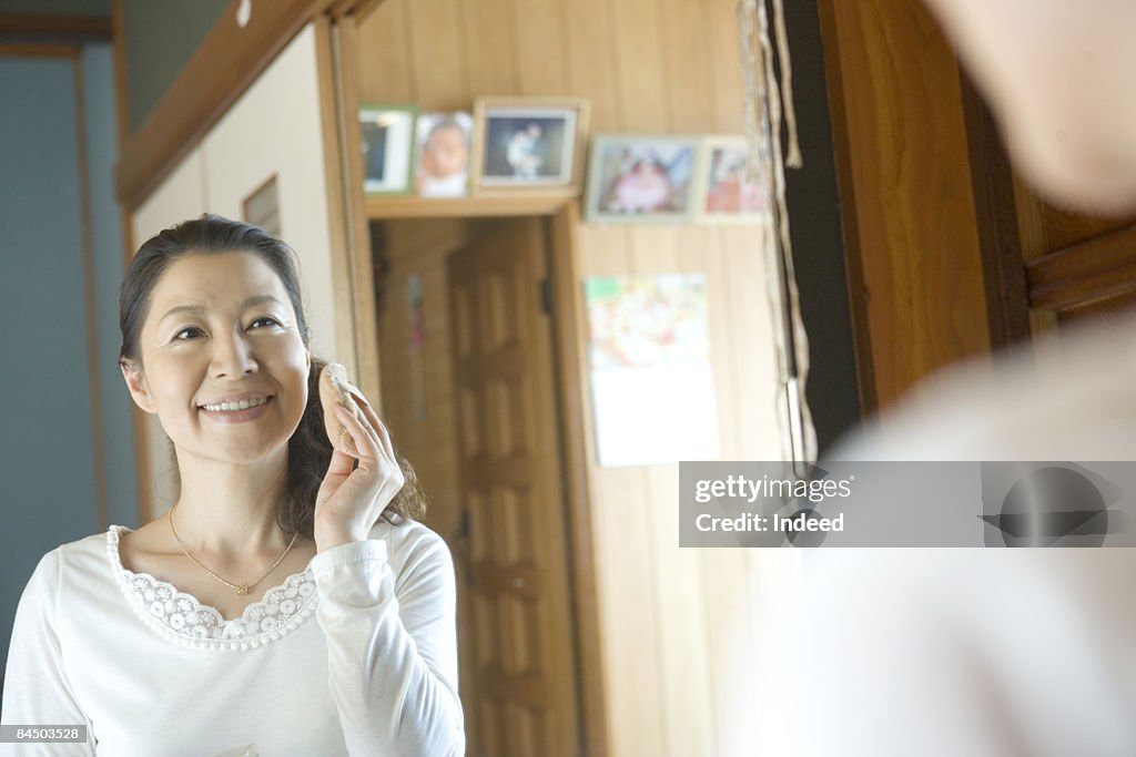 Mature woman applying makeup, looking at mirror