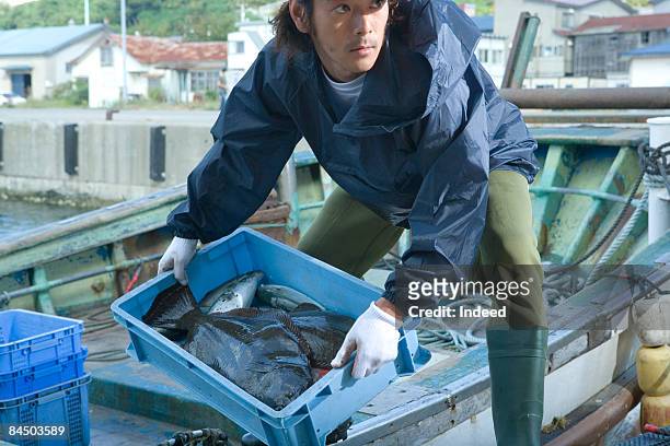 fisherman carrying crate of fish from boat - asian fishing boat stock-fotos und bilder