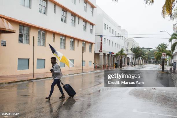 Abby Jenkins walks against the wind with her luggage and umbrella to get to safety, in Miami Beach, Fla., on Sept. 9, 2017.