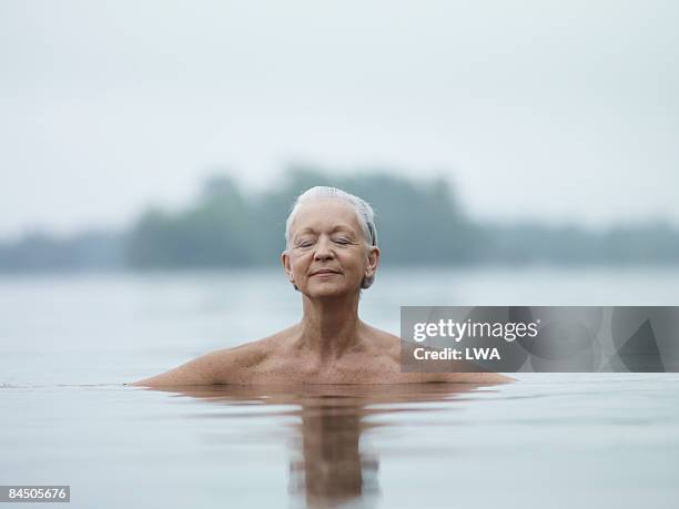 naked woman sitting in lake, eyes closed - older woman wet hair stock pictures, royalty-free photos & images