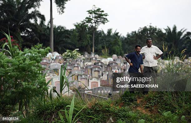 Two men watch a burial ceremony of an ethnic Indian man while standing inside a Chinese cemetery in Pouching outside the Kuala Lumpur on January 28,...