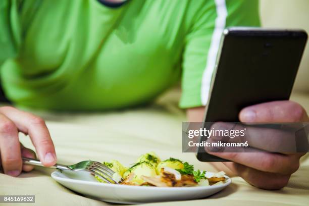 man eating dinner sitting  on bed & looking up social media on mobile phone. - unidad de entrada fotografías e imágenes de stock