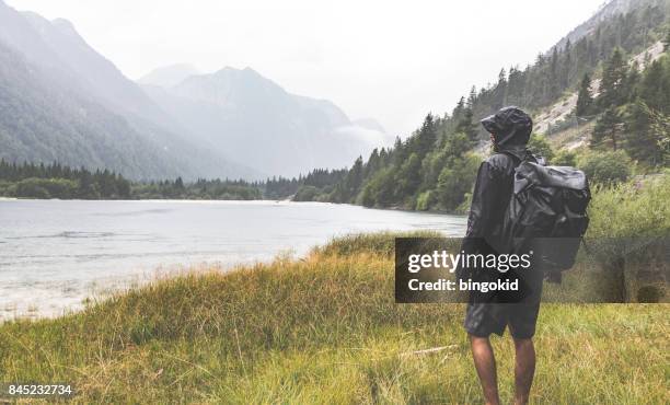 hiker with a backpack watching the lake sourrounded by mountains - windbreak stock pictures, royalty-free photos & images