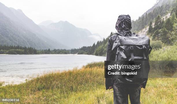 wandelaar in regenvest met kap op het kijken naar bergen en wolken - kapstaden stockfoto's en -beelden