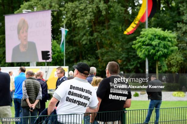 Two men wearing shirts with slogans against German Chancellor and Christian Democrat Angela Merkel stand by a fenceat a fest tent during an election...
