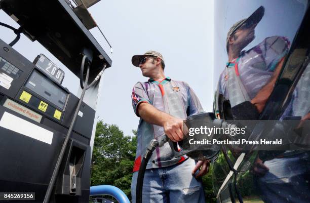 Refelcted in the side of a pickup truck, Matthew Legere, an attendant at Rinaldi Energy in Saco, pumps gas for a customer at the full service station...