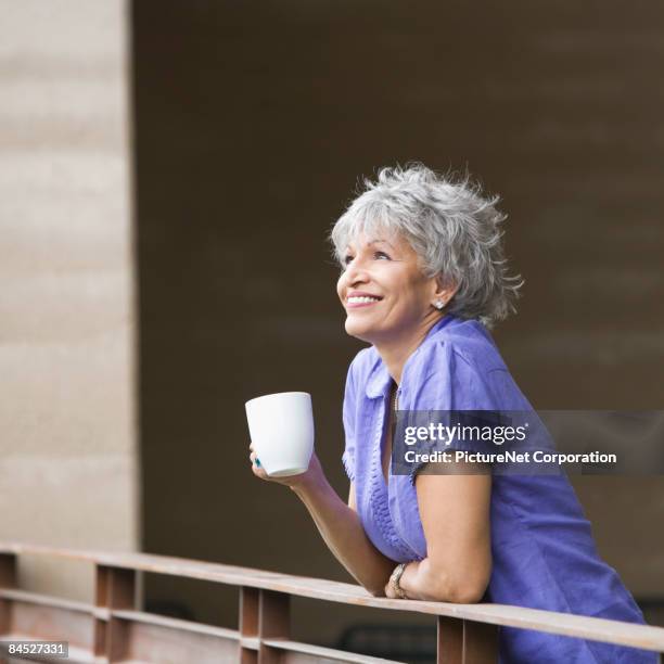 hispanic woman drinking coffee on balcony - old woman side view foto e immagini stock