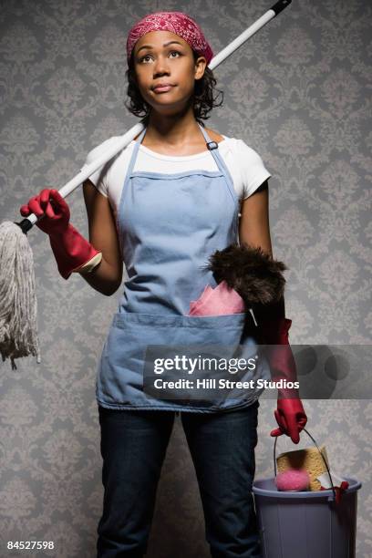 mixed race housewife standing with cleaning supplies - bored housewife stock-fotos und bilder