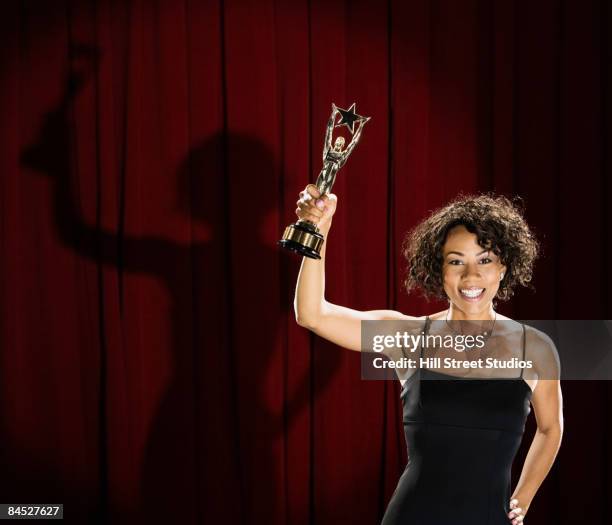 mixed race woman standing on stage with trophy - awards night fotografías e imágenes de stock