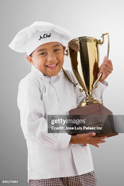 mixed race boy in chef's whites holding trophy - big cook 個照片及圖片檔