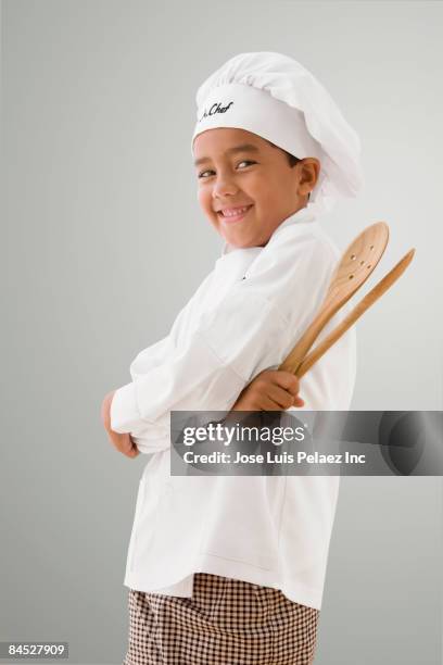 mixed race boy in chef's whites holding wooden spoons - uniforme de chef fotografías e imágenes de stock