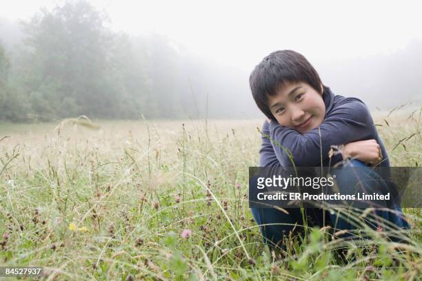 asian woman squatting in remote field - saia midi stock-fotos und bilder