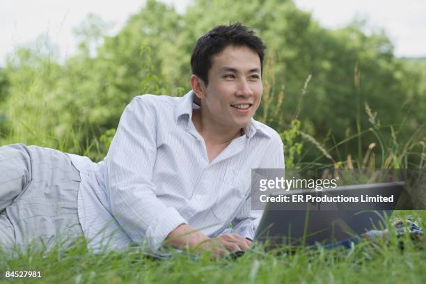 asian man laying in grass using laptop - saia midi stock-fotos und bilder