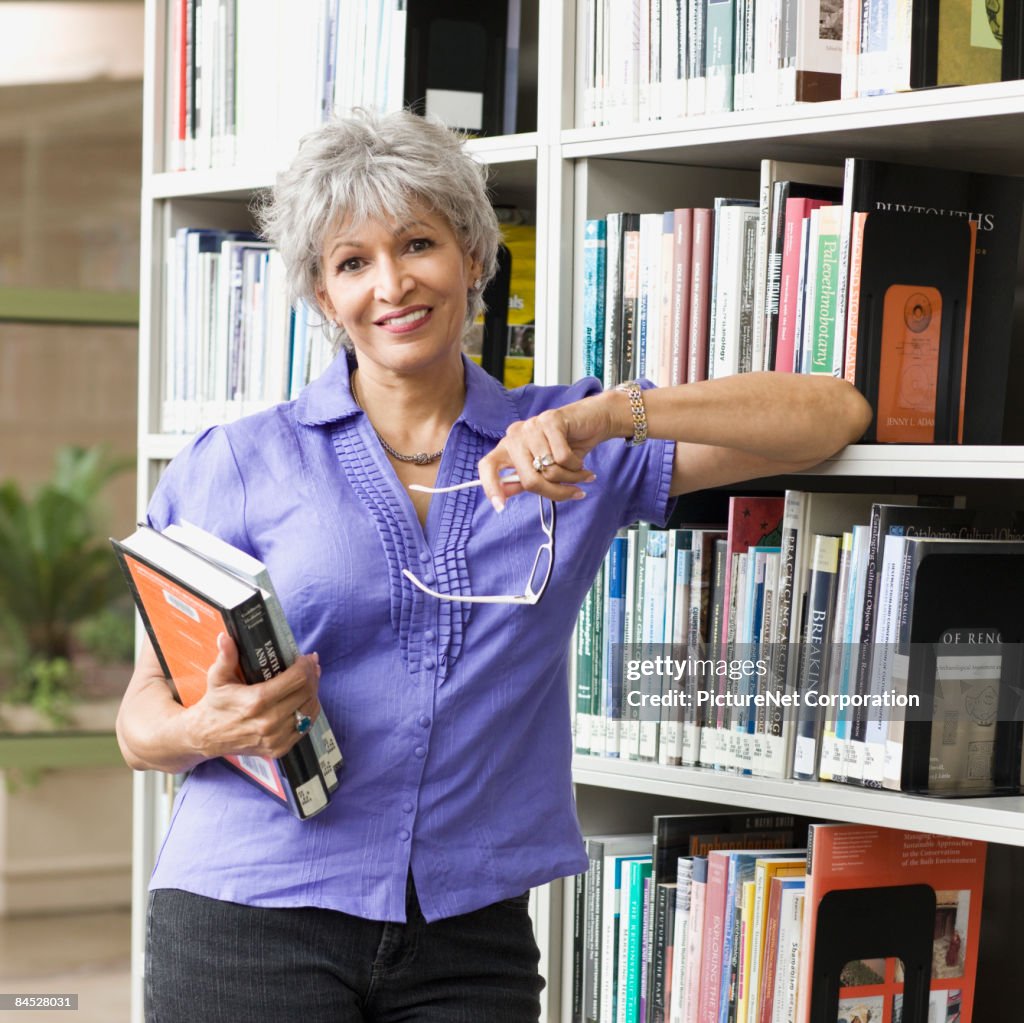 Hispanic woman holding books in library