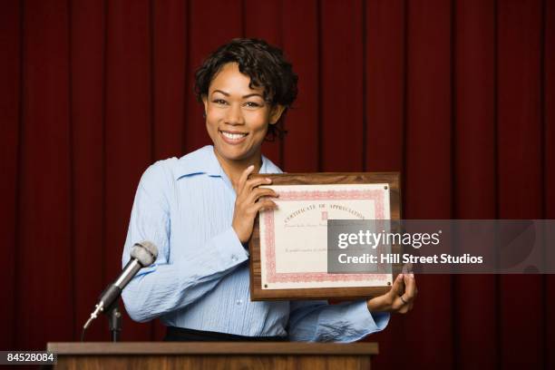 mixed race businesswoman speaking at podium with certificate - business awards ceremony stock pictures, royalty-free photos & images